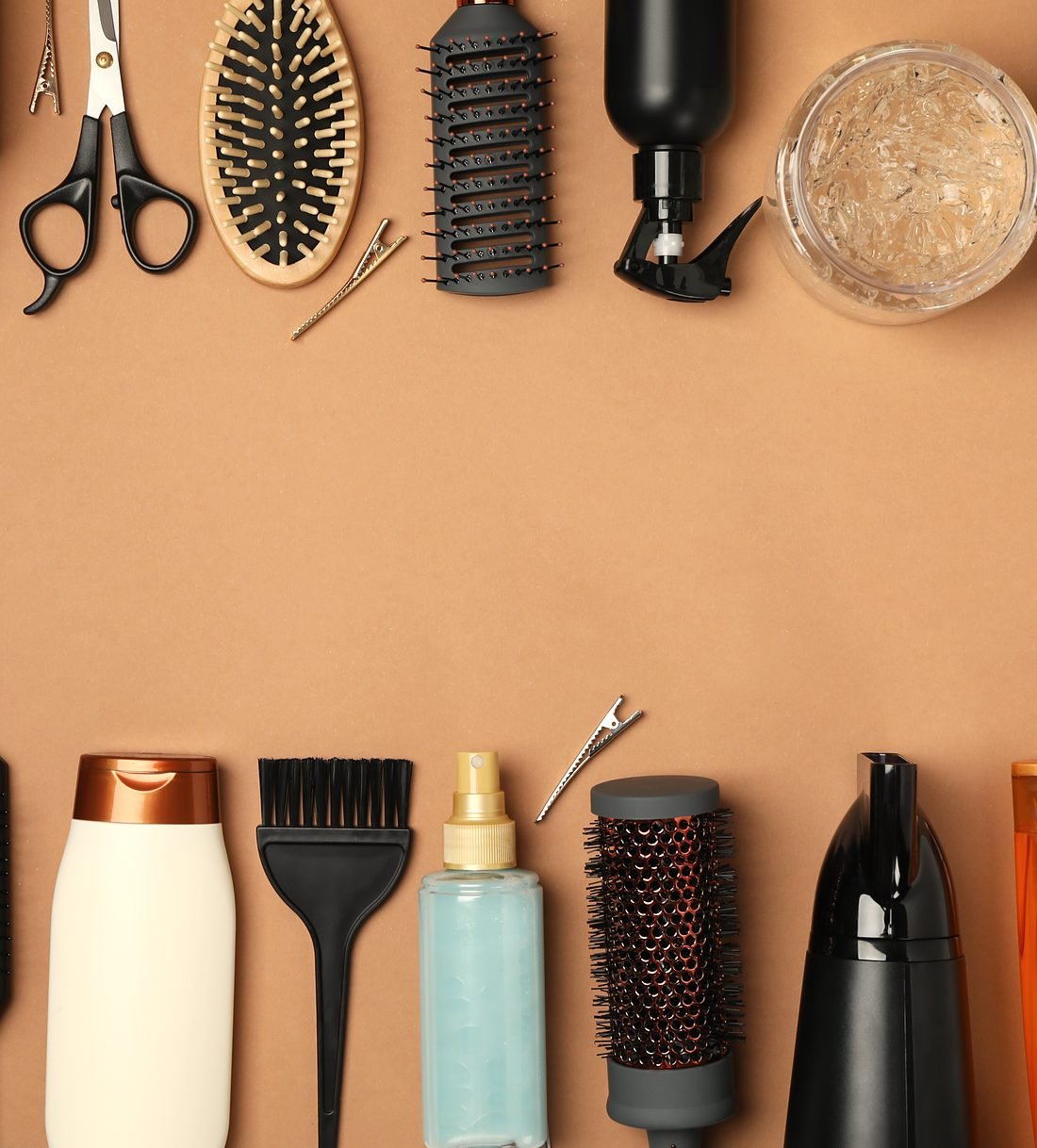 Brushes, combs, scissors and haircare bottles laid out on warm tan paper